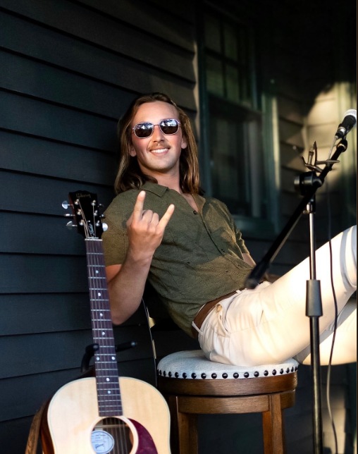 Brandon Stone Jr. in sunglasses on a porch with his acoustic guitar between songs