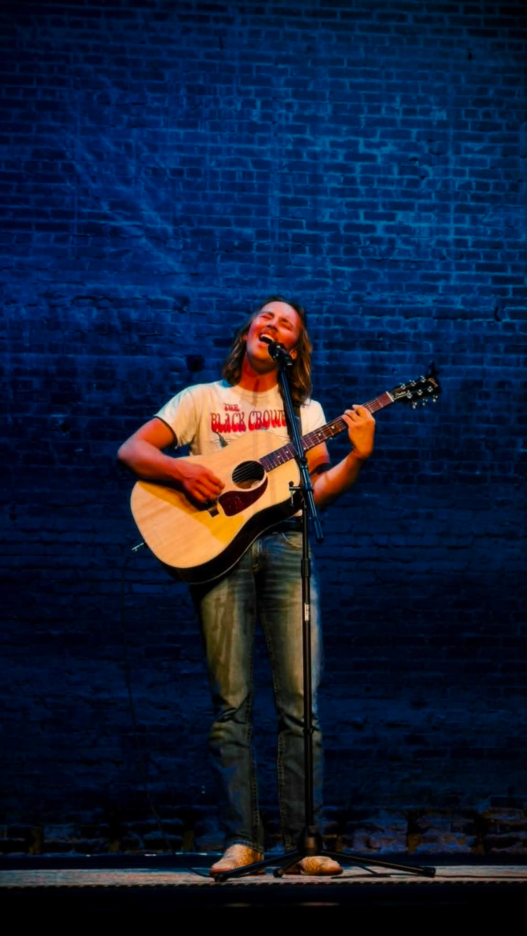 Brandon Stone Jr. singing into the mic under deep blue stage lights at a live show