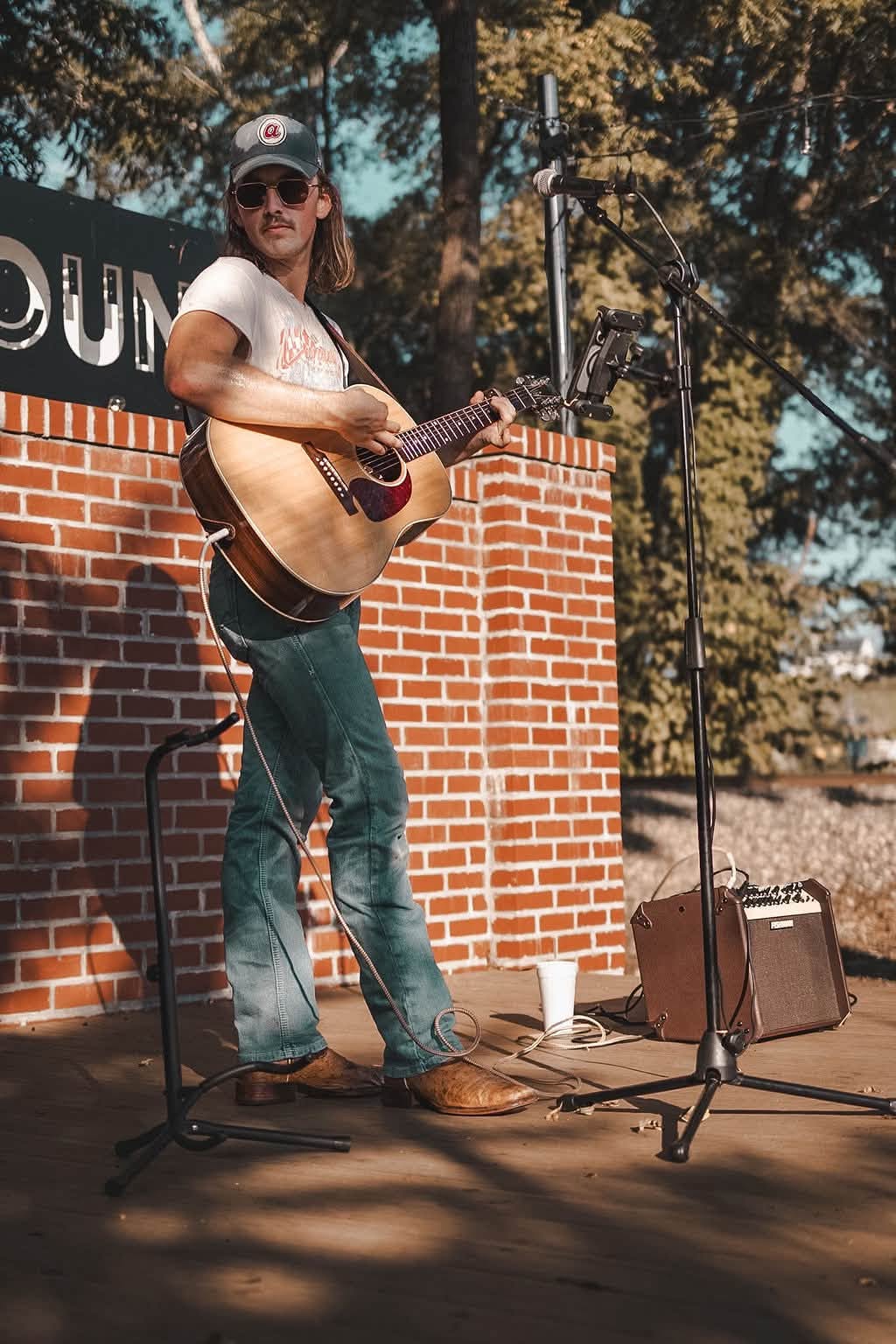 Brandon Stone Jr. standing with his acoustic guitar in front of a red brick wall