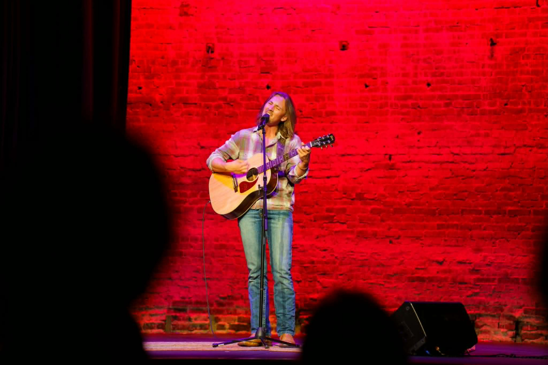 Brandon Stone Jr. playing electric guitar on stage in front of a red-lit brick wall