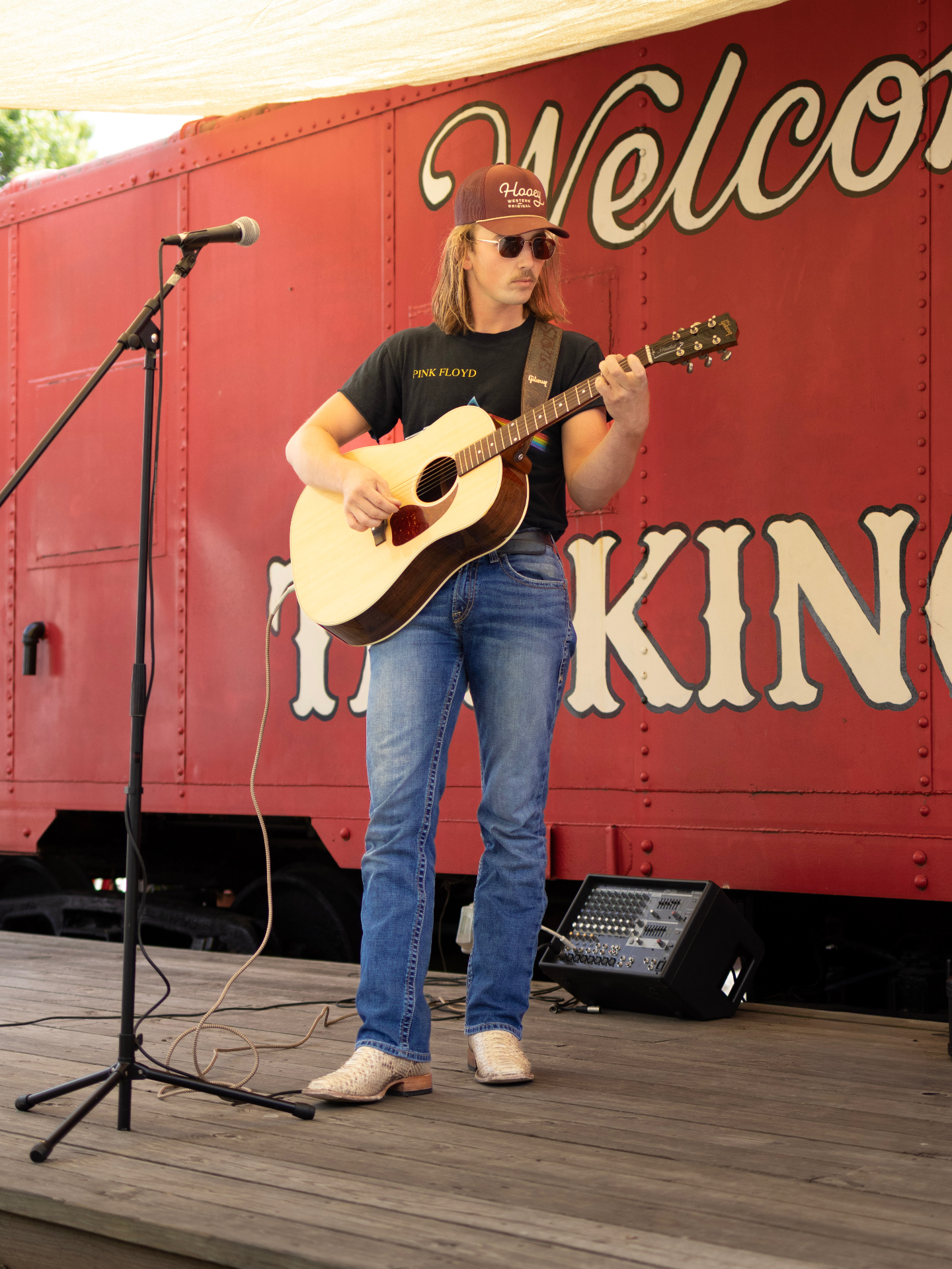 Brandon Stone Jr. with his acoustic guitar beside a vintage red train car in North Georgia