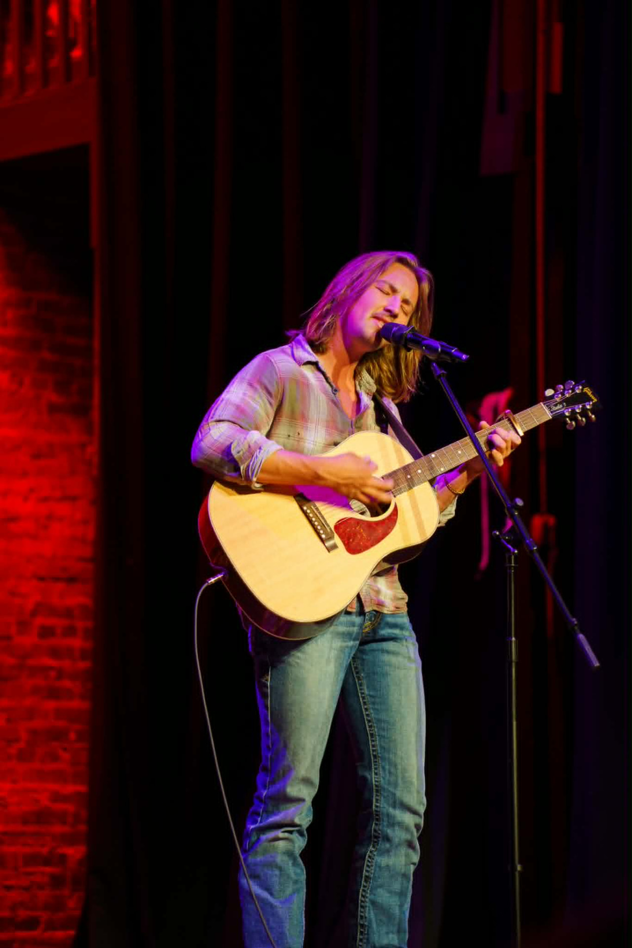 Side profile of Brandon Stone Jr. playing acoustic guitar in purple stage light